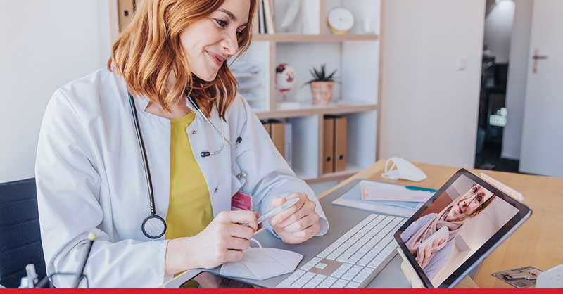 Nurse sitting at desk talking to someone on an tablet