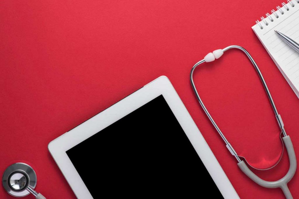 iPad, stethoscope, notebook and pen with red background