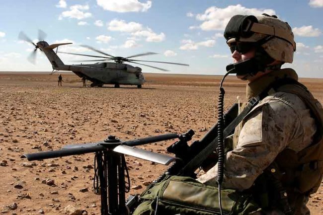 military in desert with helicopter in background