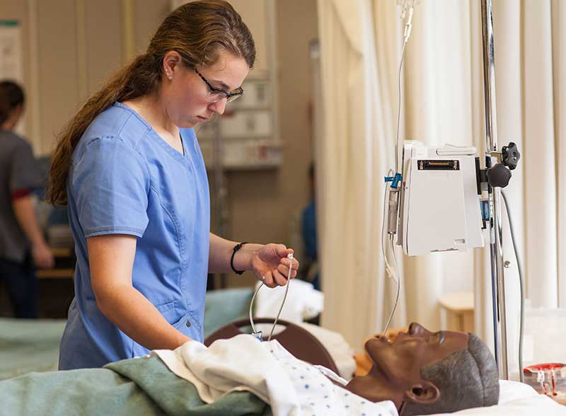 nursing student in scrubs working with sim manikin