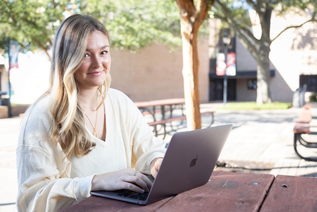 student sitting outside at table using laptop