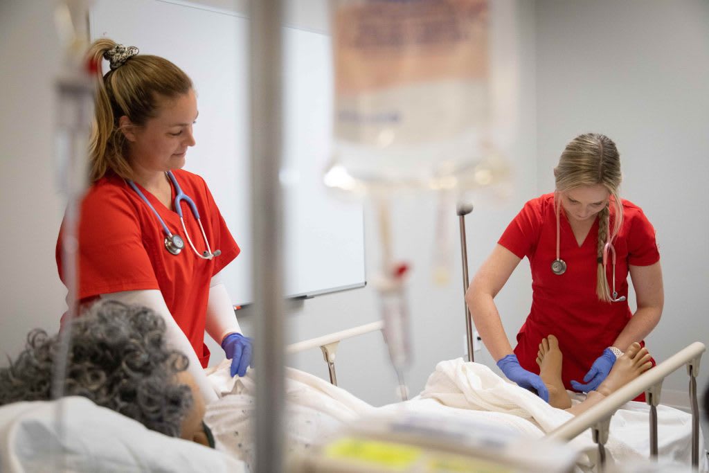 two UST nursing students working in sim lab