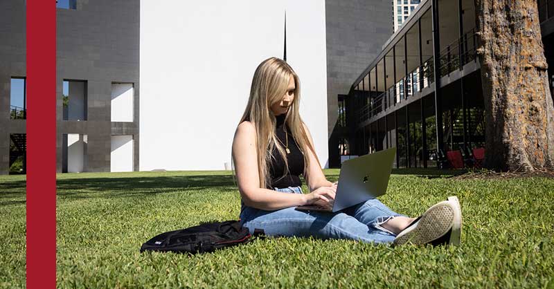 student sitting outside in grass working on a laptop