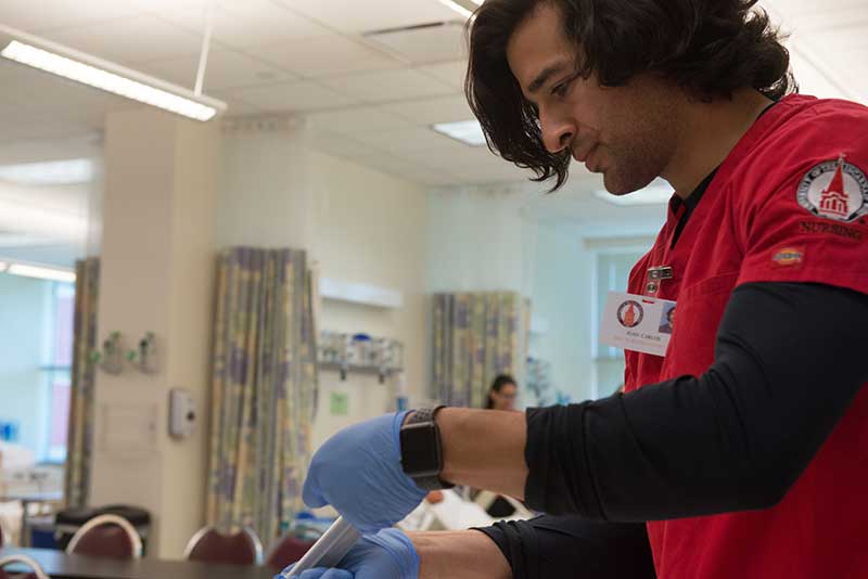 male nursing student in UIW scrubs examining syringe