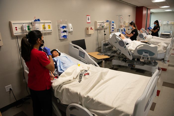 UIW ABSN student in red scrubs using stethoscope on manikin