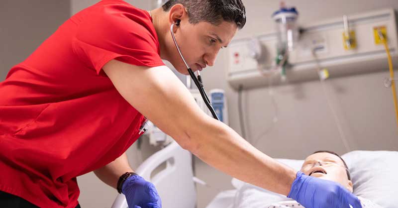 Nurse in red scrubs working with sim manikin