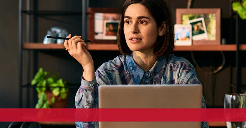 woman sitting at desk holding a pen while working on laptop