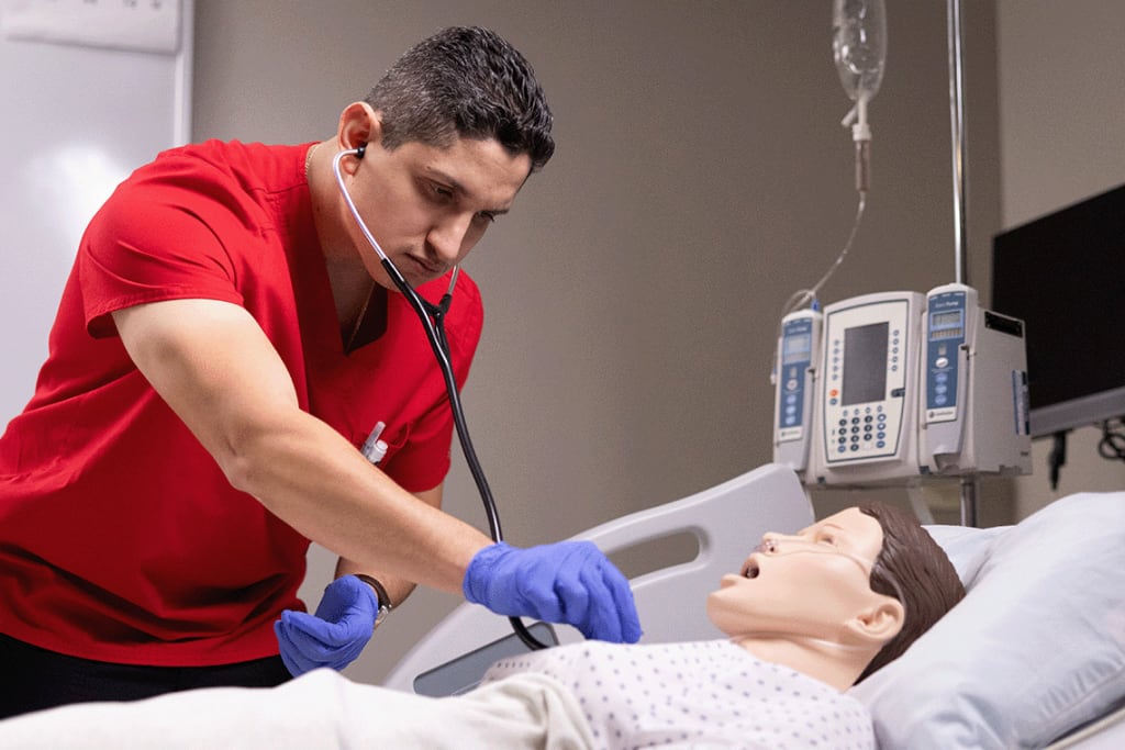 UIW nursing student in red scrubs and stethoscope in lab setting