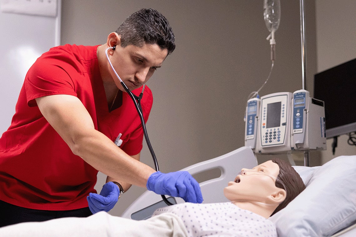 UIW nursing student in scrubs and stethoscope working on a manikin