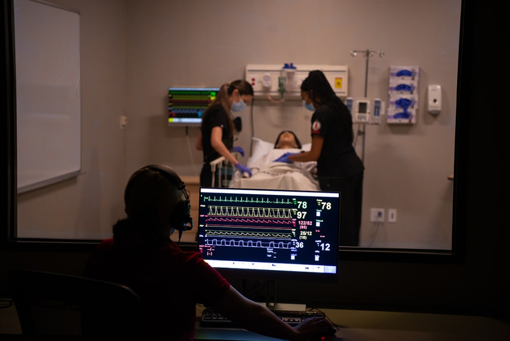 Clinical setting with monitors and students practicing nursing techniques