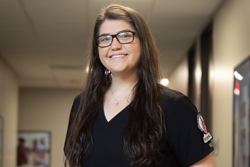 UIW student smiling in scrubs and glasses