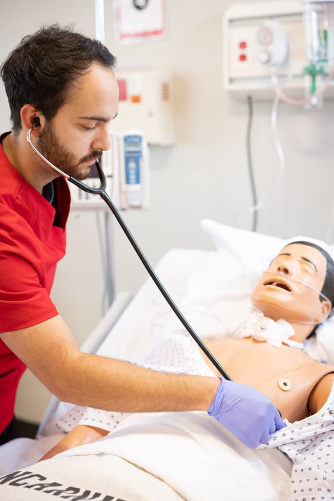 UIW student wearing stethoscope practicing on manikin
