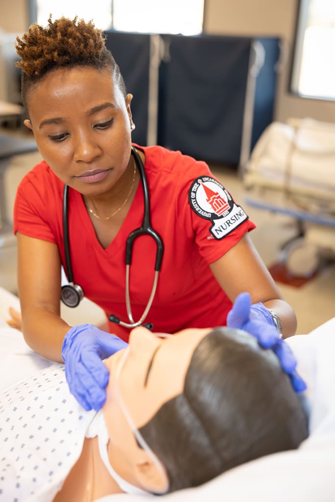 UIW nursing student working on a manikin in red scrubs