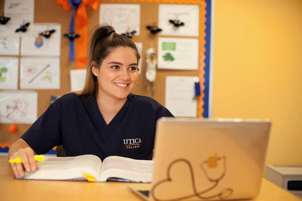 Utica student working on computer with a textbook