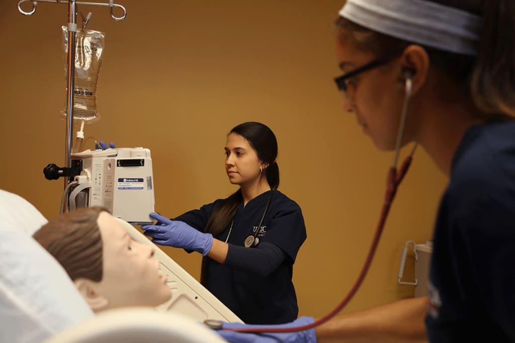 Utica student in stethoscope working with another student on a manikin