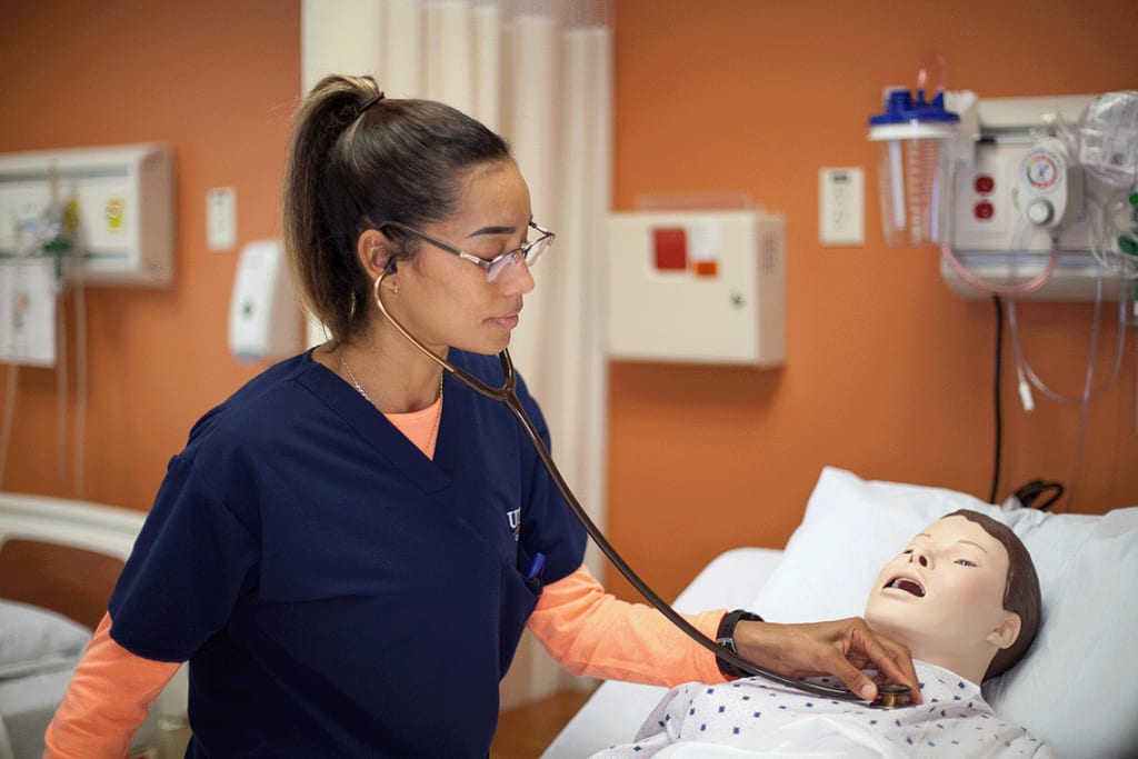 Nursing student with stethoscope working on a manikin