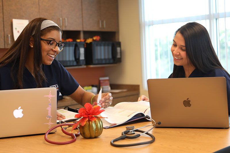 Two ABSN students studying together at desk with their laptops