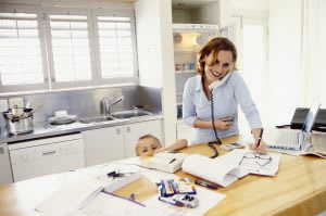 Woman on the phone with her advisor and helping her child in the kitchen.