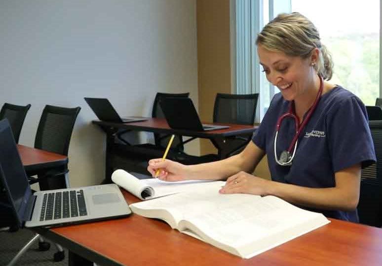 Nursing student studying with textbook and computer