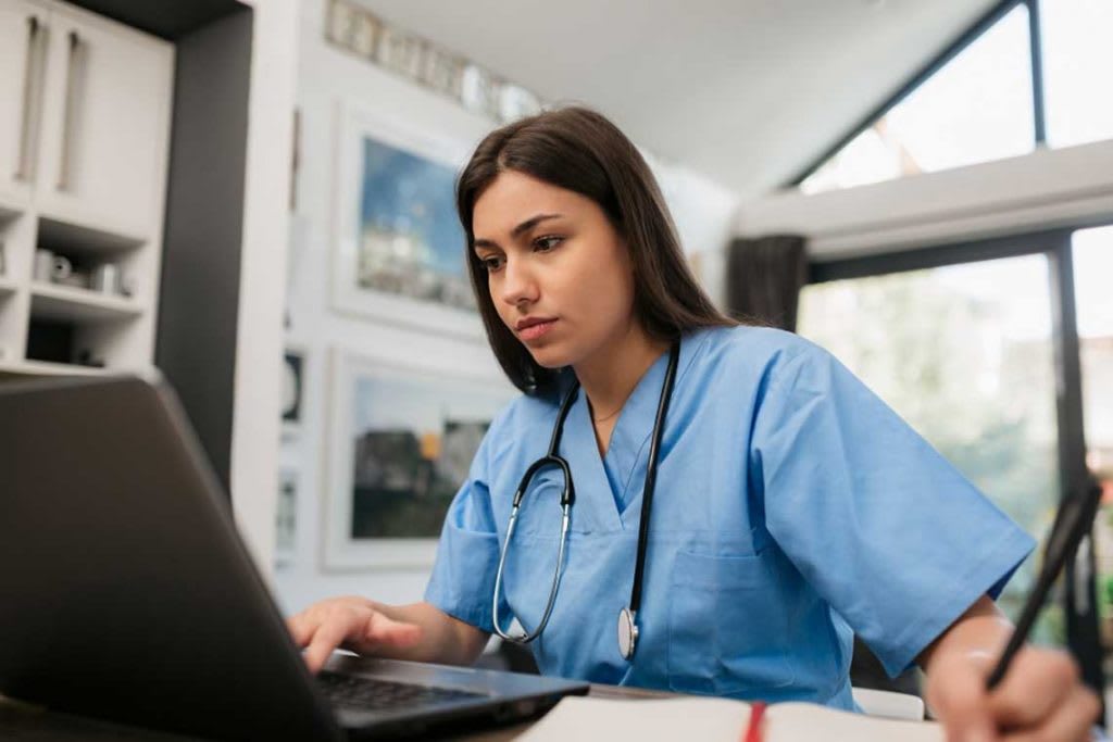 nurse sitting at desk working on laptop