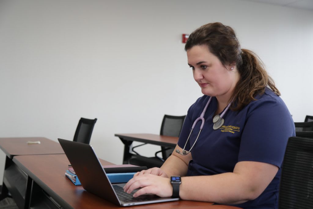 a nursing student sitting at a desk using a laptop