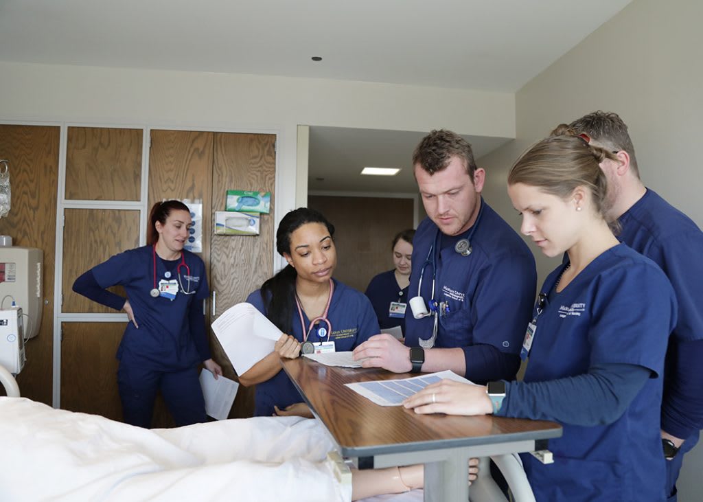 Marian ABSN students looking at paperwork in sim lab