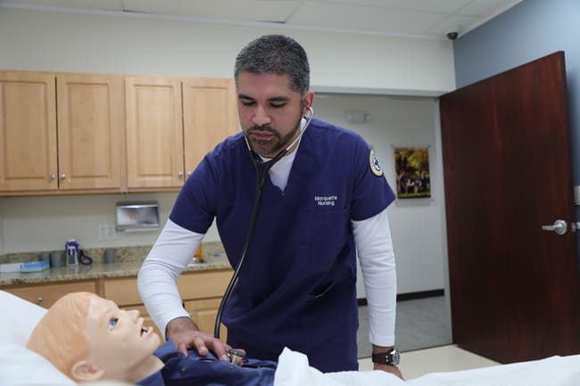 a marquette student listening to a simulation manikin's heartbeat