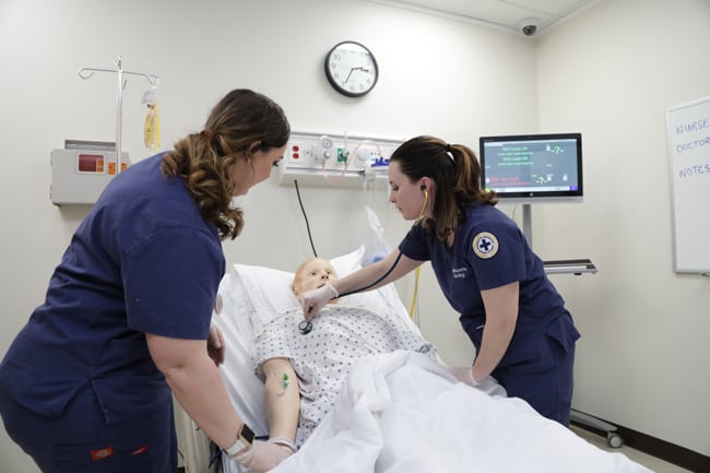 Two marquette students examining a simulation manikin