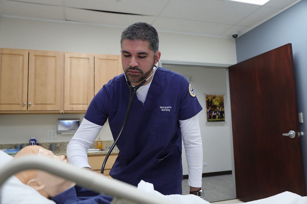 nursing student with stethoscope practicing on manikin