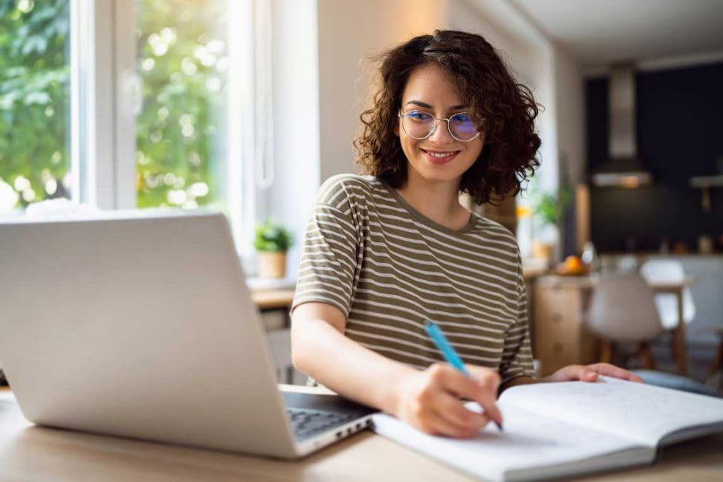 woman writing and using laptop