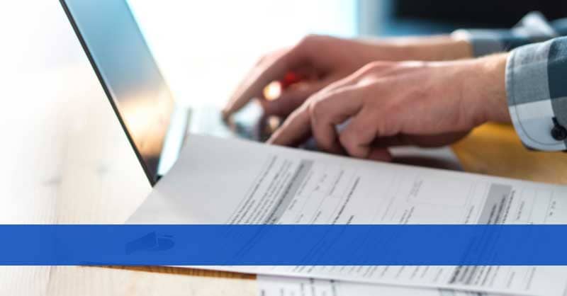 Person's hands shown working on a laptop with sheets of paper