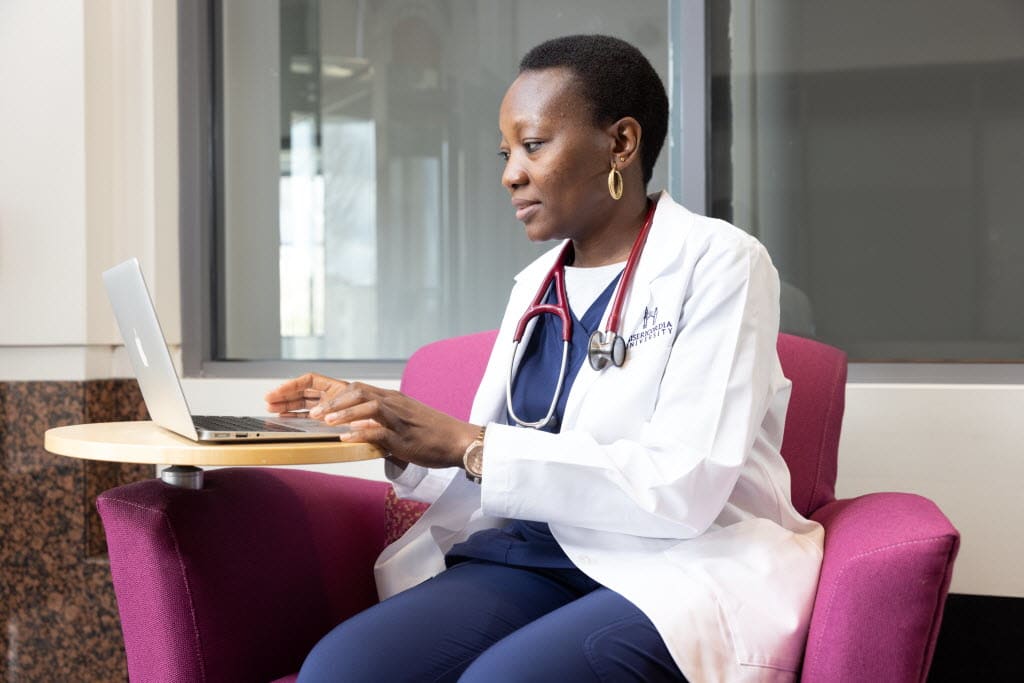 nursing student in white coat sitting and using laptop