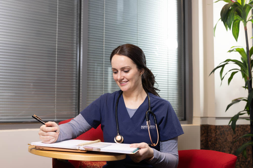 student in chair with table looking at notebook smiling