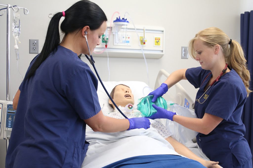two Marian ABSN students working together with a sim manikin in simulation lab