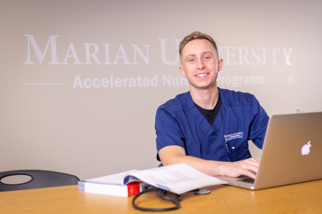 smiling ABSN student sitting at desk using laptop