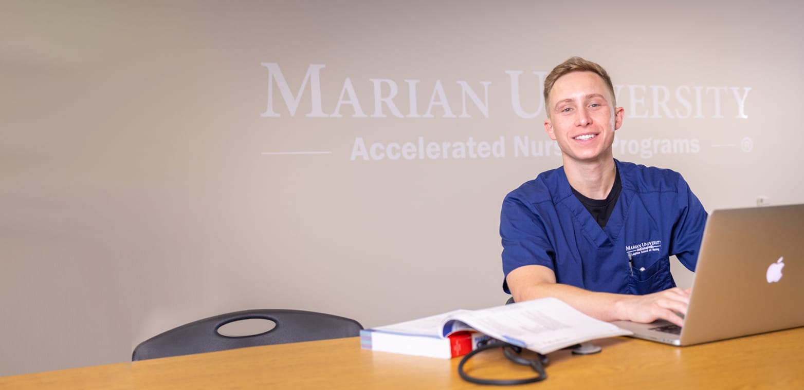 a Marian ABSN student sitting at table using laptop