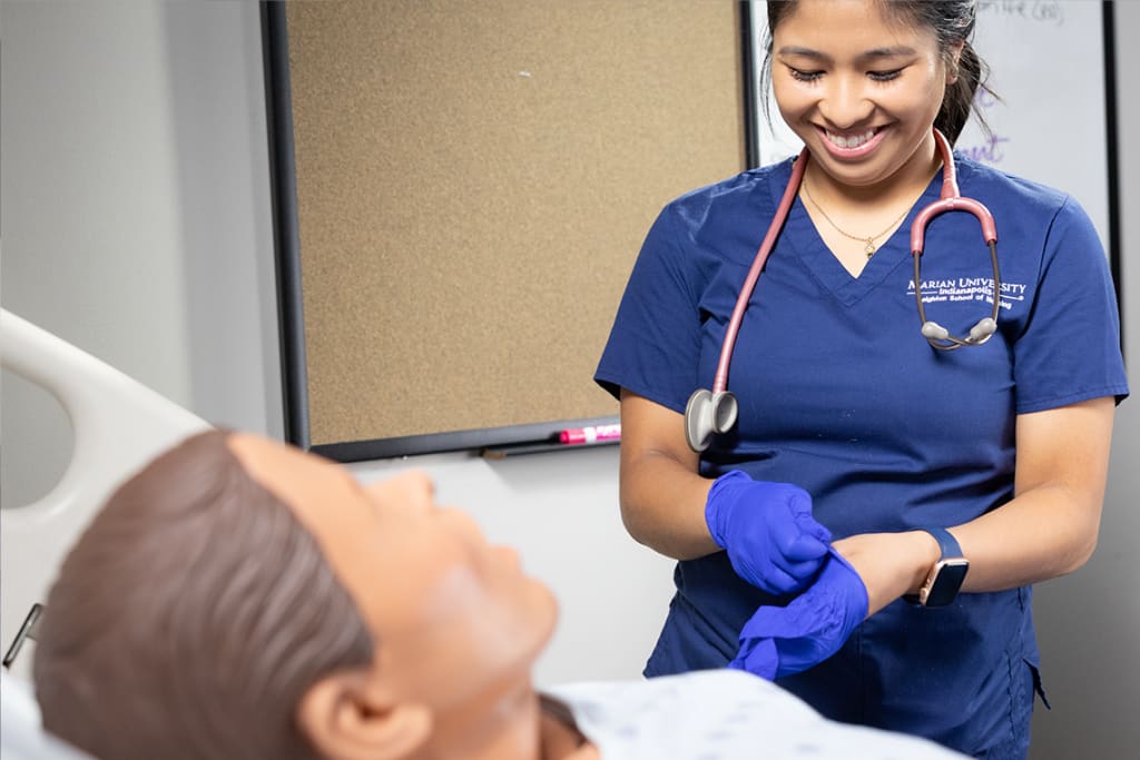 smiling marian student putting gloves on over manikin