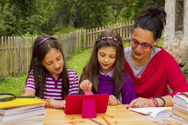 Adult watching children learn and play on tablet outdoors