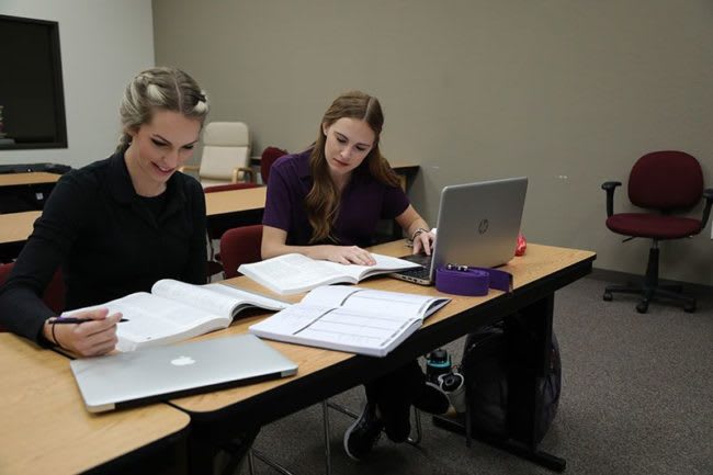 two OTA students studying together with books and laptops