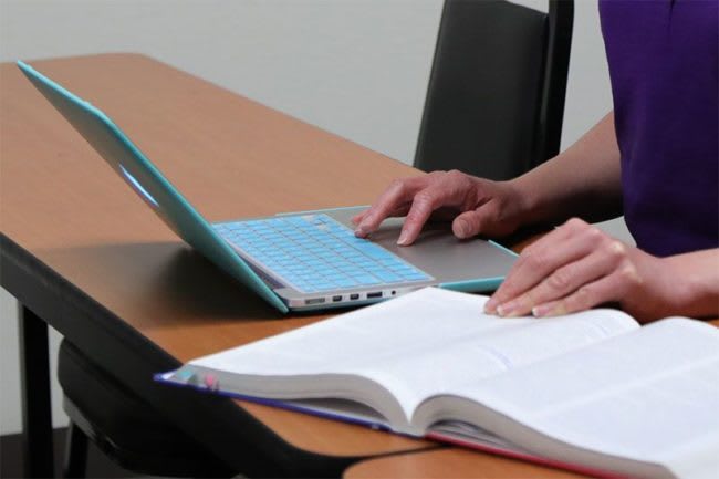 student sitting at desk studying with laptop and textbook