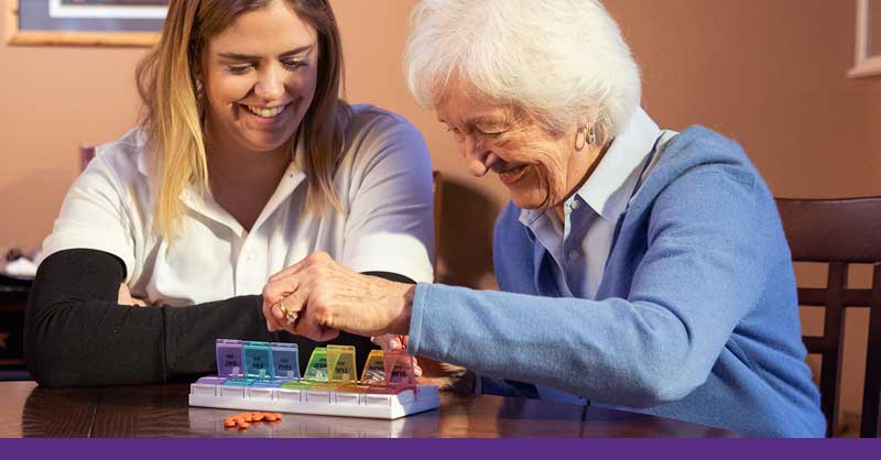 Woman sitting with elderly patient helping with daily pills