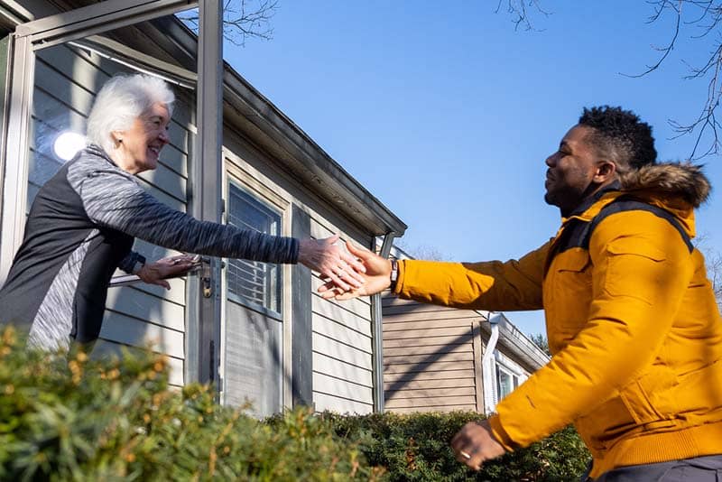 man shaking the hand of an elderly woman outside at her front door