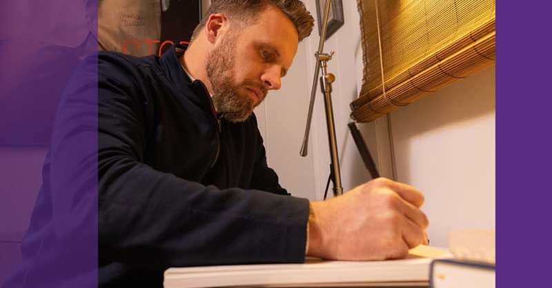 man sitting at desk writing notes