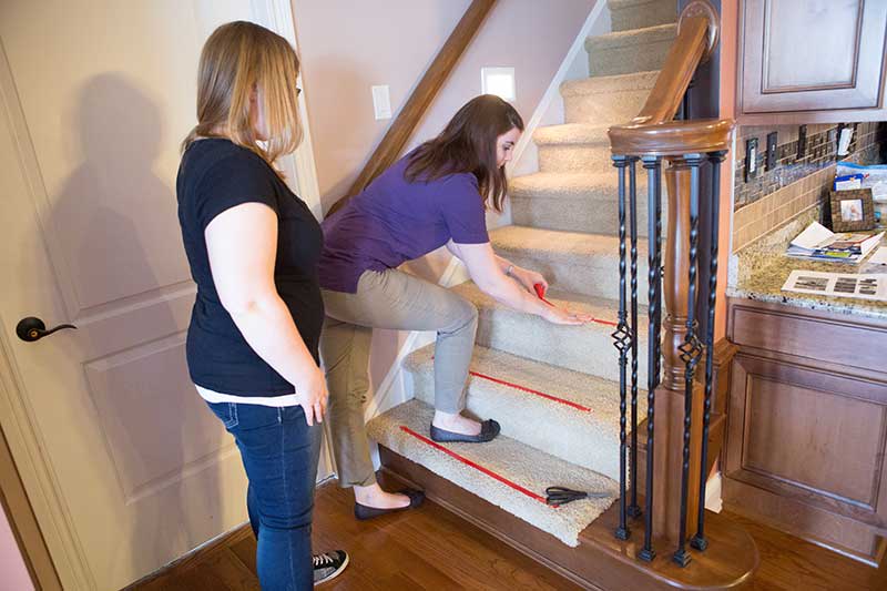 woman placing red tape on stair steps in woman's home