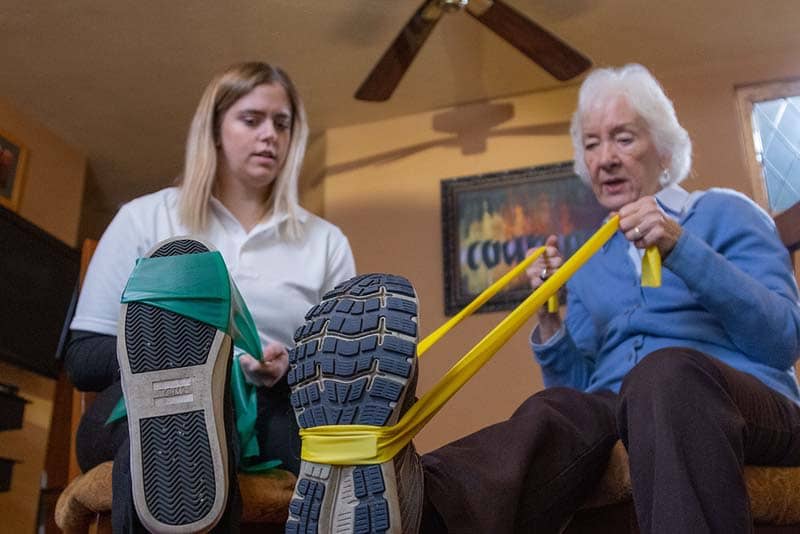 student helping elderly woman with stretch bands on her feet