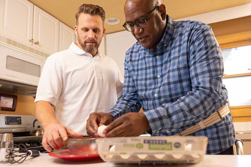 OT student with older man in kitchen helping crack an egg