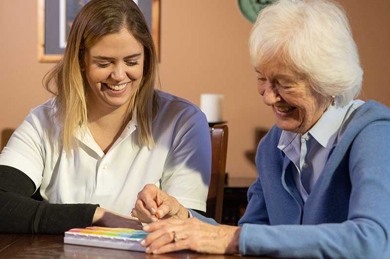 OT student sitting at desk with elderly woman filling a pill divider