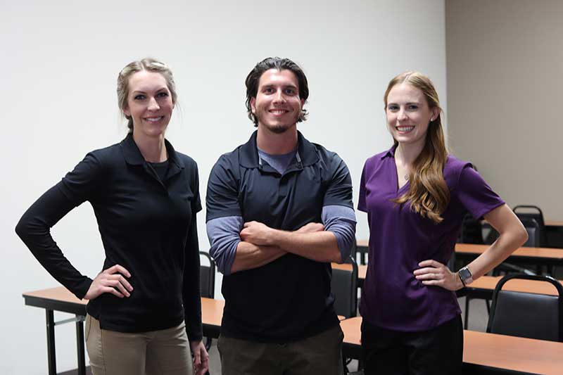 three OT students posing and smiling in class