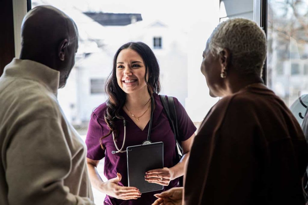 woman wearing scrubs greeting two elderly patients