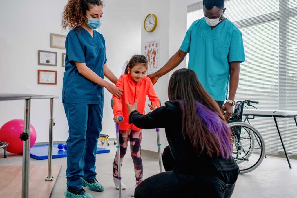 adults with nurse helping child with physical therapy